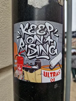 Graffiti-style sticker featuring the phrase "Keep on Rising" along with spray paint cans, a paint roller, and a fire extinguisher. The sticker has a urban art vibe and promotes a message of perseverance.