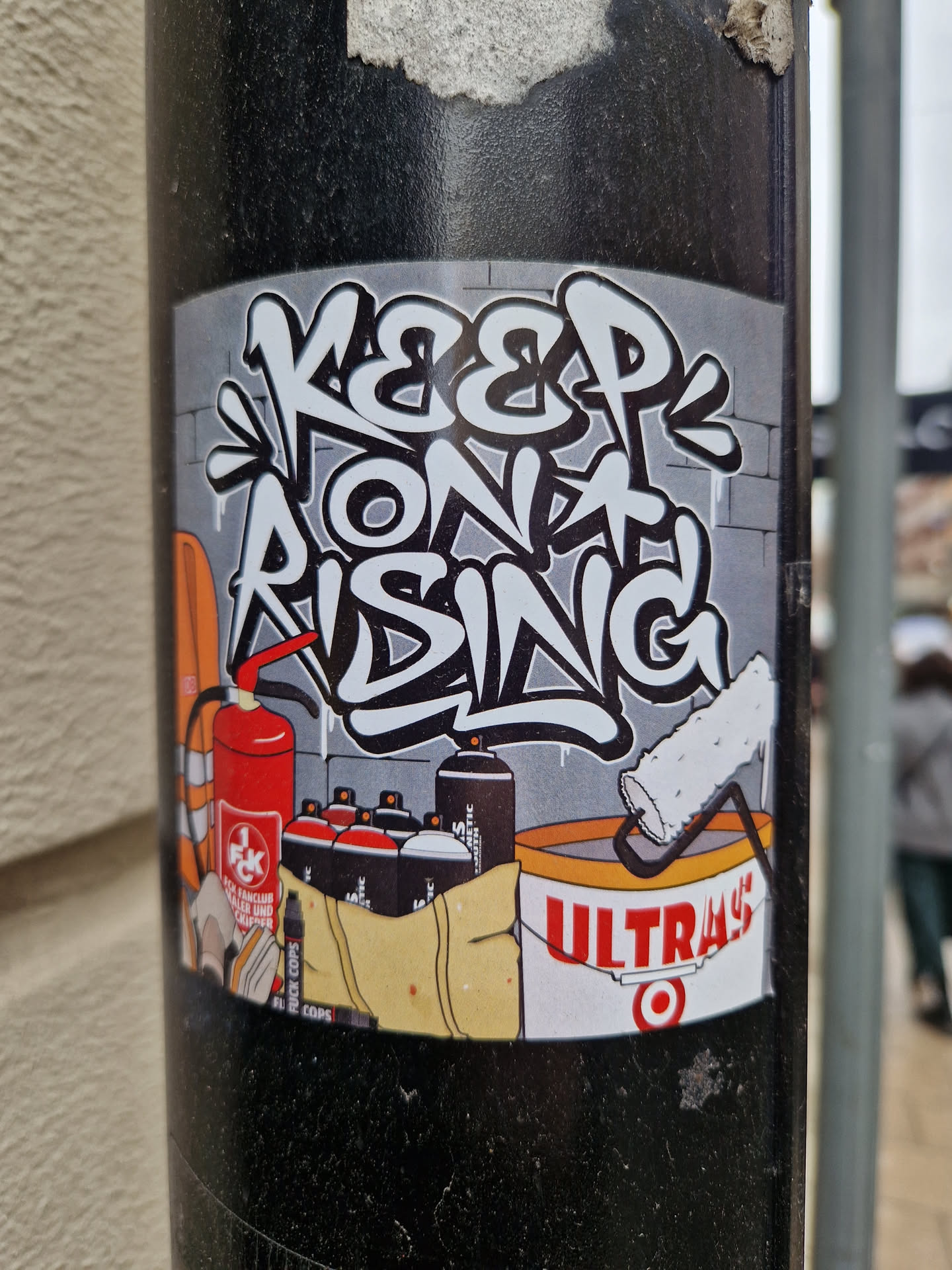 Graffiti-style sticker featuring the phrase "Keep on Rising" along with spray paint cans, a paint roller, and a fire extinguisher. The sticker has a urban art vibe and promotes a message of perseverance.