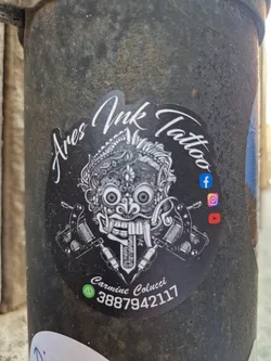 Black and white sticker with a Barong mask illustration, tattoo machines, and contact info. 