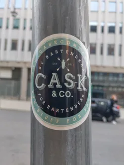 A round sticker with a dark-blue background and light-green circular border.  It features the logo for Cask & Co., a company that provides products for bartenders.  The text on the sticker reads "www.caskcompany.com by bartenders for bartenders est. 2011 cask & co. ".  A cocktail shaker icon is also present in the design.