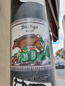 A sticker featuring a boar and several figures in green clothing. The text 'Skitiga hajen' is visible at the top.  The numbers 40 and 11 are visible on the clothing of two figures.
