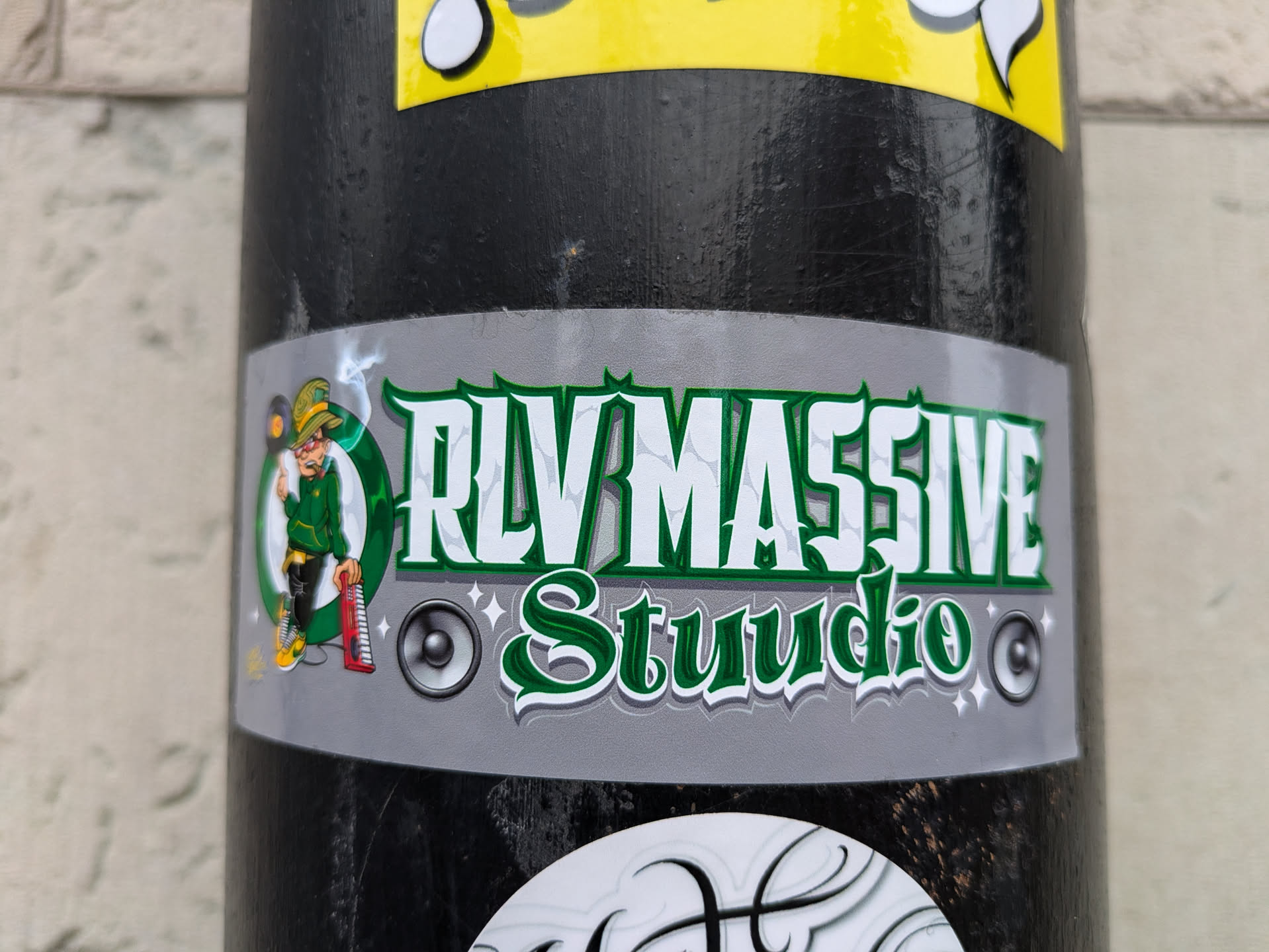 A sticker featuring the logo of RLV MASSIVE Studio. The logo includes a cartoon leprechaun playing a keyboard, along with the studio name in stylized green lettering on a gray background. The style is reminiscent of a music studio or record label.
