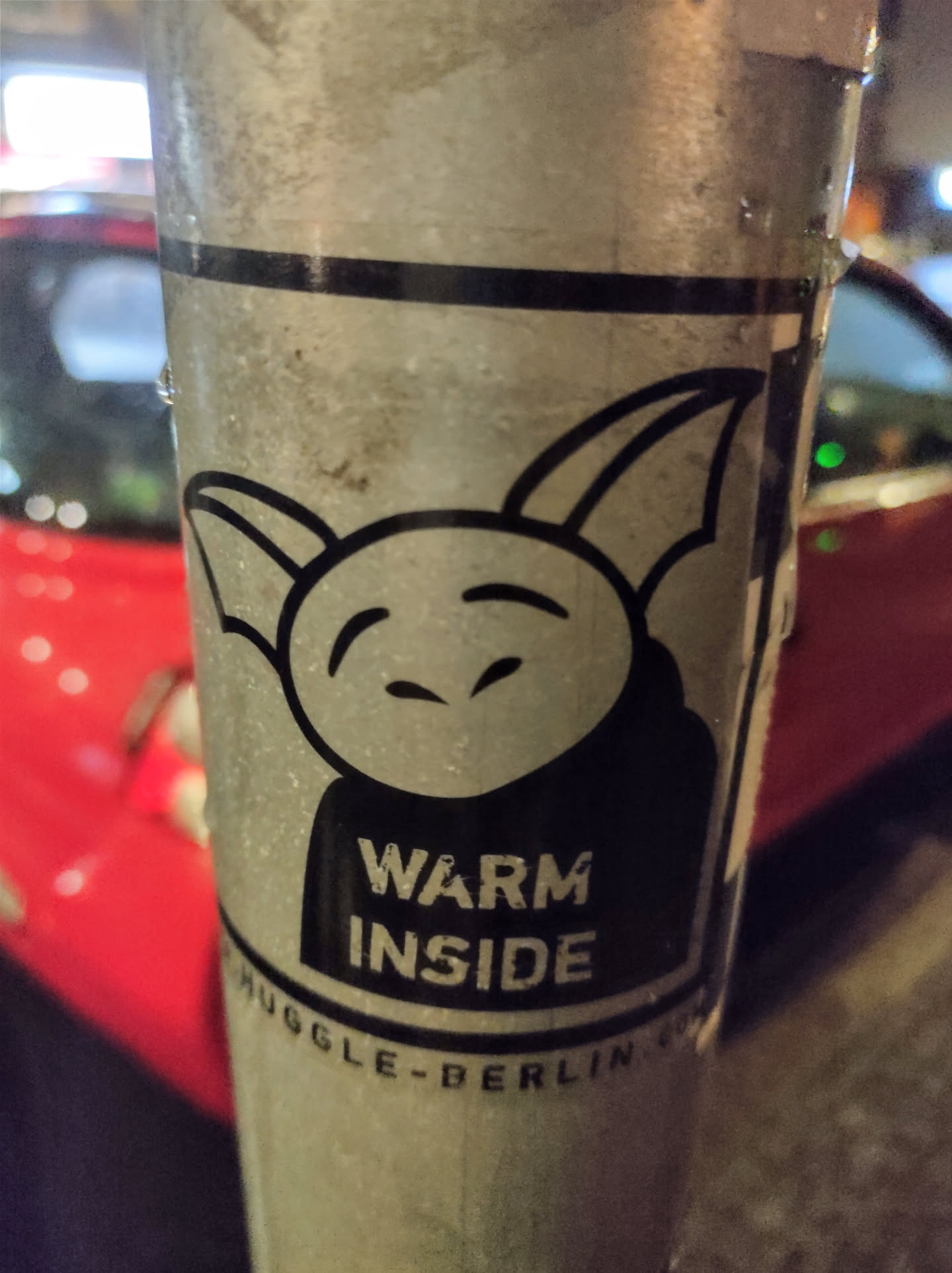 A sticker featuring a simple cartoon character with small horns or ears, a round face, and a slightly mischievous expression. The text "WARM INSIDE" is prominently displayed below the character. The sticker also includes the text "MUGGLE-BERLIN" at the bottom. The character appears friendly and somewhat whimsical.