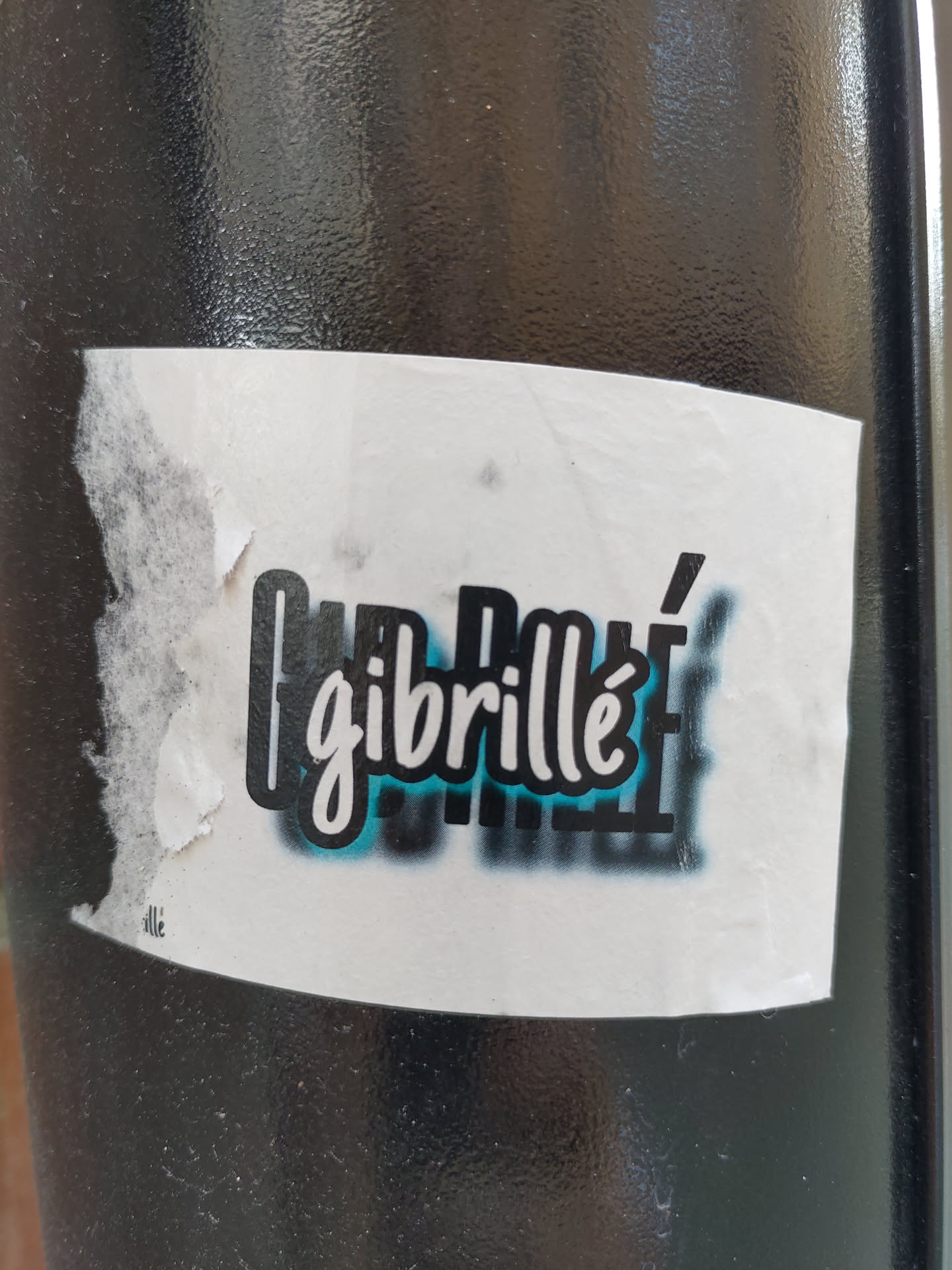 A sticker featuring the word "Gibrillé" in stylized lettering with a teal and black color scheme.  The sticker is slightly damaged at one corner.