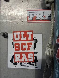 Red and white sticker with the text "ULTSCF RAS" in a bold, college-style font.  There are some additional black and white graphic elements on the sticker as well as the text "/RTS.PNF\K432".