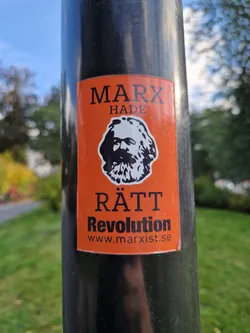 An orange sticker with a picture of Karl Marx. The text on the sticker says "Marx hade rätt" which translates to "Marx was right" in Swedish. It also says "Revolution" and provides a website address: www.marxist.se