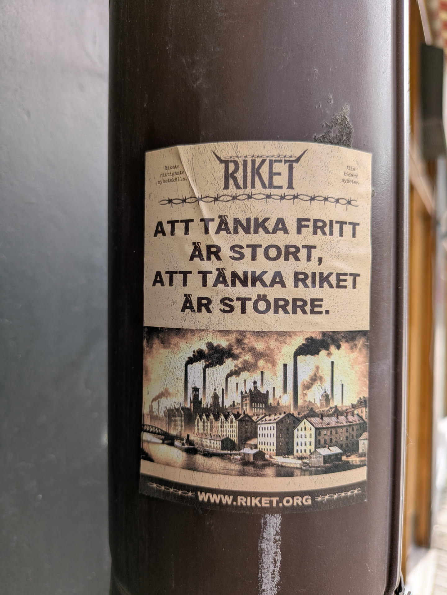 The sticker features the text: "Att tänka fritt är stort, att tänka riket är större." It also includes an image of a city with smokestacks and the URL www.riket.org.