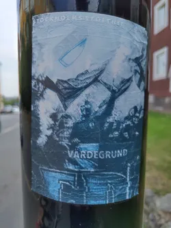 A sticker featuring a stylized image, possibly referencing Stockholm's history or culture. The central motif appears to be a historical scene with figures and a boat, rendered in shades of blue and grey.  The text 'Vardegrund' is visible at the bottom.