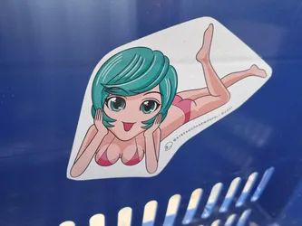 A sticker featuring an illustration of a young woman with teal hair, lying on her stomach, wearing a pink bikini. The art style is reminiscent of anime or manga.  The sticker has a copyright notice that includes the year 2021.