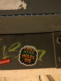 Street sticker A die-cut sticker with a white border featuring vibrant, stylized text set against a dark backdrop framed by dark green cannabis leaves. The text reads 'I ROLL' in warm orange and yellow, 'HASH' in bright green tones, and 'HOLES 916' in dripping orange and golden hues. Above the main graphic, an Instagram handle '@i_roll_hashholes_916' is printed in small black text along the upper edge.