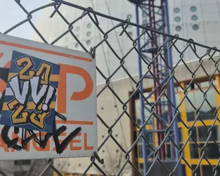A rectangular sticker with stylized 'VV' lettering and the numbers '24' and '23' is pasted on an orange and white 'P' parking sign. The sticker is in a navy blue square with an orange border. The word 'ANGEL' is written below with black marker with a tick.