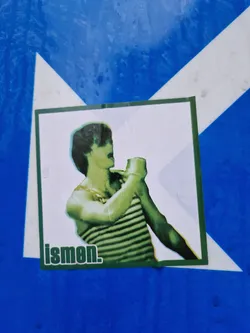 A sticker featuring a stylized image of a man in a striped shirt. The word 'ismen.' is printed at the bottom. The sticker has a vintage or retro aesthetic. The image is in shades of green.