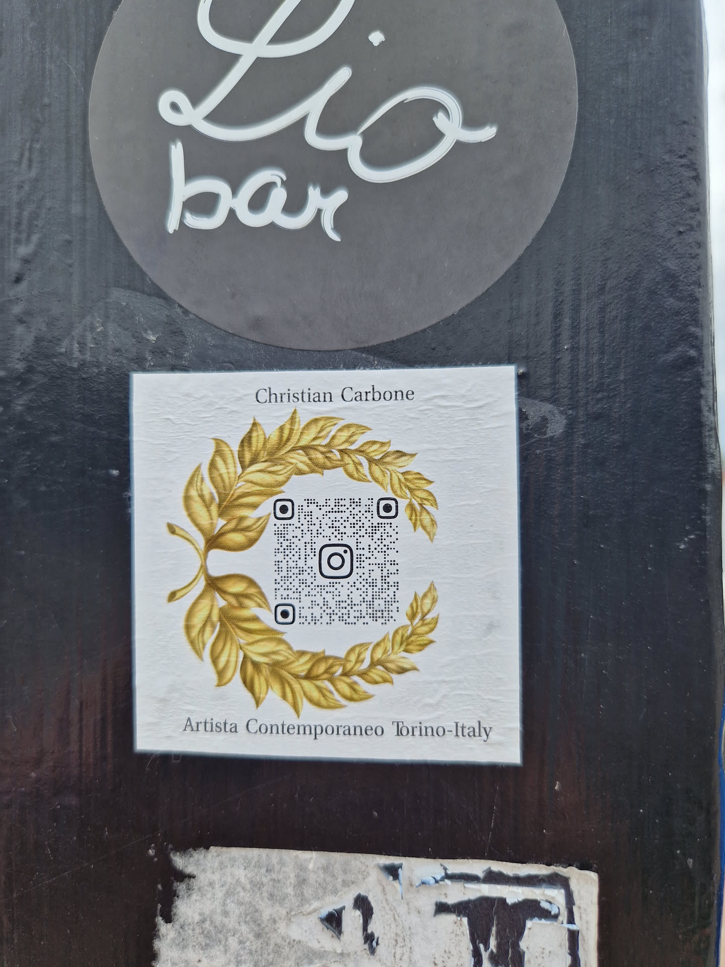 Sticker featuring a QR code surrounded by a golden laurel wreath. The artist's name and location are mentioned at the bottom. 