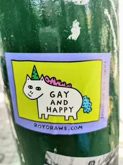 A sticker featuring a cartoon unicorn with a party hat, wearing a pink mane and a blue tail. The text "Gay and Happy" is written on the sticker, along with the website roydraws.com. 