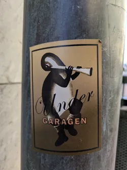 A rectangular sticker featuring a stylized creature playing a long, thin horn. The creature is primarily black with white shading. The background of the sticker is a golden brown color. Below the creature, the word "Under" is written in cursive black font, and below that, the word "GARAGEN" is written in block letters in a light orange color.