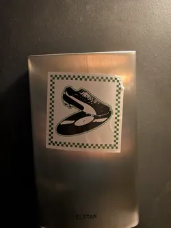 Street sticker A square sticker featuring an illustration of a classic football cleat resting atop a black vinyl record, bound together by a green outline. The central graphic is set against a white background and enclosed by a dark green and white checkerboard border.