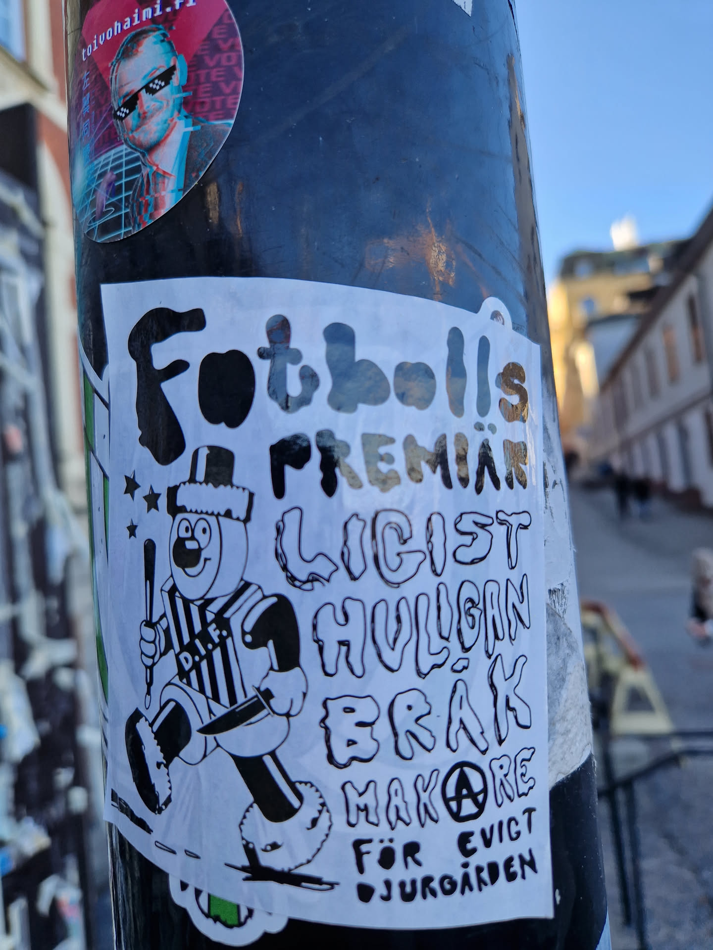 A sticker featuring a cartoon character holding a stick and knife, with text suggesting a football premiere, hooligans, and eviction from Djurgården. The style is reminiscent of protest or punk graphics.