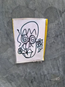 A hand-drawn sticker featuring a whimsical character with swirling eyes, a unique hairstyle, and what appears to be a cigarette in its mouth. The artist's tag, MOET ONE, is visible on the sticker.