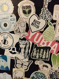 A collection of stickers featuring various designs, including a heart-shaped sticker that says "Boss Bitch", praying hands, an alien, and a variety of other illustrations and text. The stickers are arranged on a dark surface, and there is some overlap.