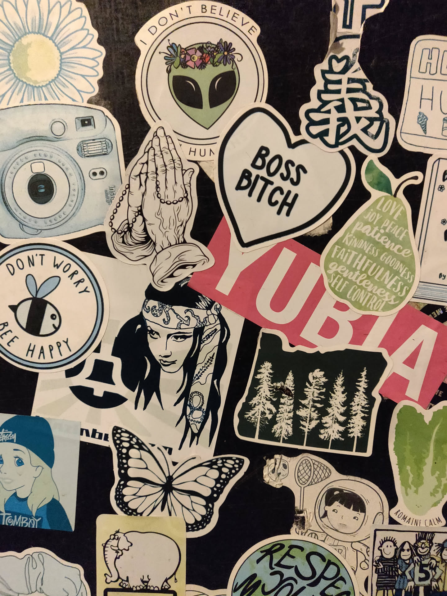 A collection of stickers featuring various designs, including a heart-shaped sticker that says "Boss Bitch", praying hands, an alien, and a variety of other illustrations and text. The stickers are arranged on a dark surface, and there is some overlap.