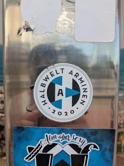 The sticker features a circular design with the text "HALBWELT ARMINEN" around the upper half and "2020" at the bottom, separated by dots. The center contains the letter "A" in white, surrounded by a design of blue and black shapes.