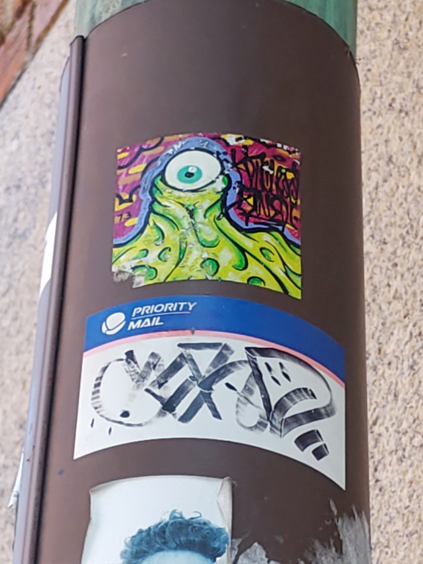 A vibrant sticker featuring a psychedelic, one-eyed creature with tentacles. The creature is predominantly green and yellow, set against a background of multicolored graffiti-style elements.  The style is reminiscent of 1990s cartoons or underground comix.