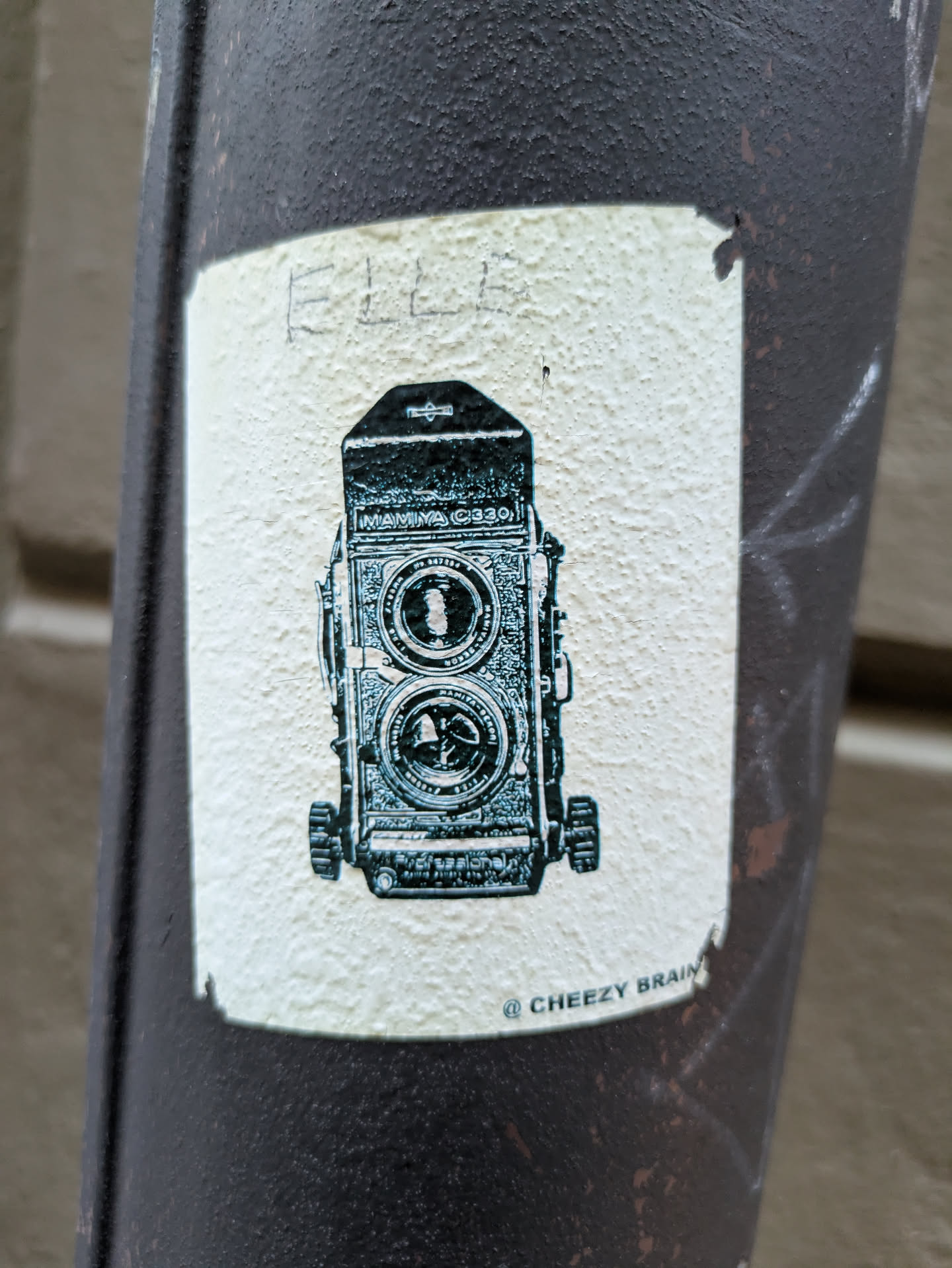 A sticker featuring a drawing of a vintage Rolleiflex camera. The sticker is off-white with teal-colored illustration and has the text "© CHEEZY BRAIN" at the bottom.