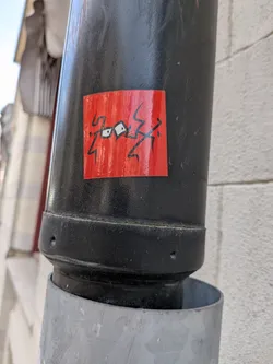 The sticker is rectangular with a vibrant, slightly textured red background. It features a bold, abstract design in black. The central elements are two white-outlined black shapes that strongly resemble stylized eyes, connected by a thin black line. Surrounding these 'eyes' are jagged, angular black lines that extend outwards, giving the impression of lightning bolts, energy, or a chaotic scribble. The overall aesthetic is graphic and minimalist, relying on strong color contrast and dynamic lines.
