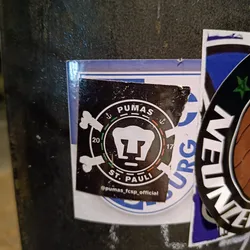 A sticker featuring a collaboration between Puma and St. Pauli. The design is black and white with a central image of a puma's head within a circular emblem. The numbers 20 and 17 flank the puma head, and anchors are incorporated into the design. The text 'PUMAS' and 'ST. PAULI' are visible. The sticker also includes the Instagram handle @pumas_fcsp_official.