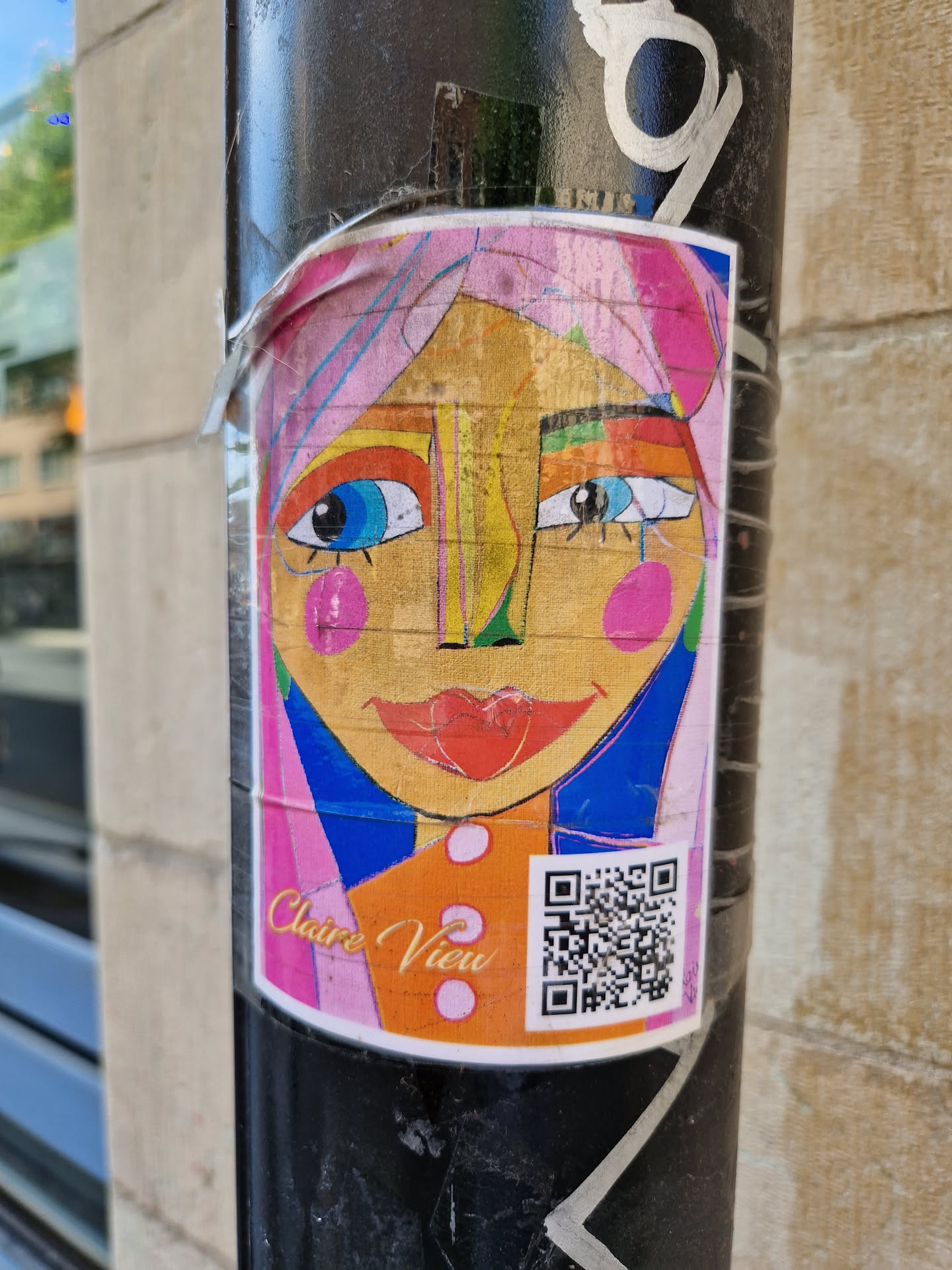 A vibrant sticker featuring a stylized female face with bold colors and abstract shapes. The artist's name, Claire View, is subtly printed at the bottom, along with a QR code. The face has pink hair, large colorful eyes and pink circles on the cheeks. 