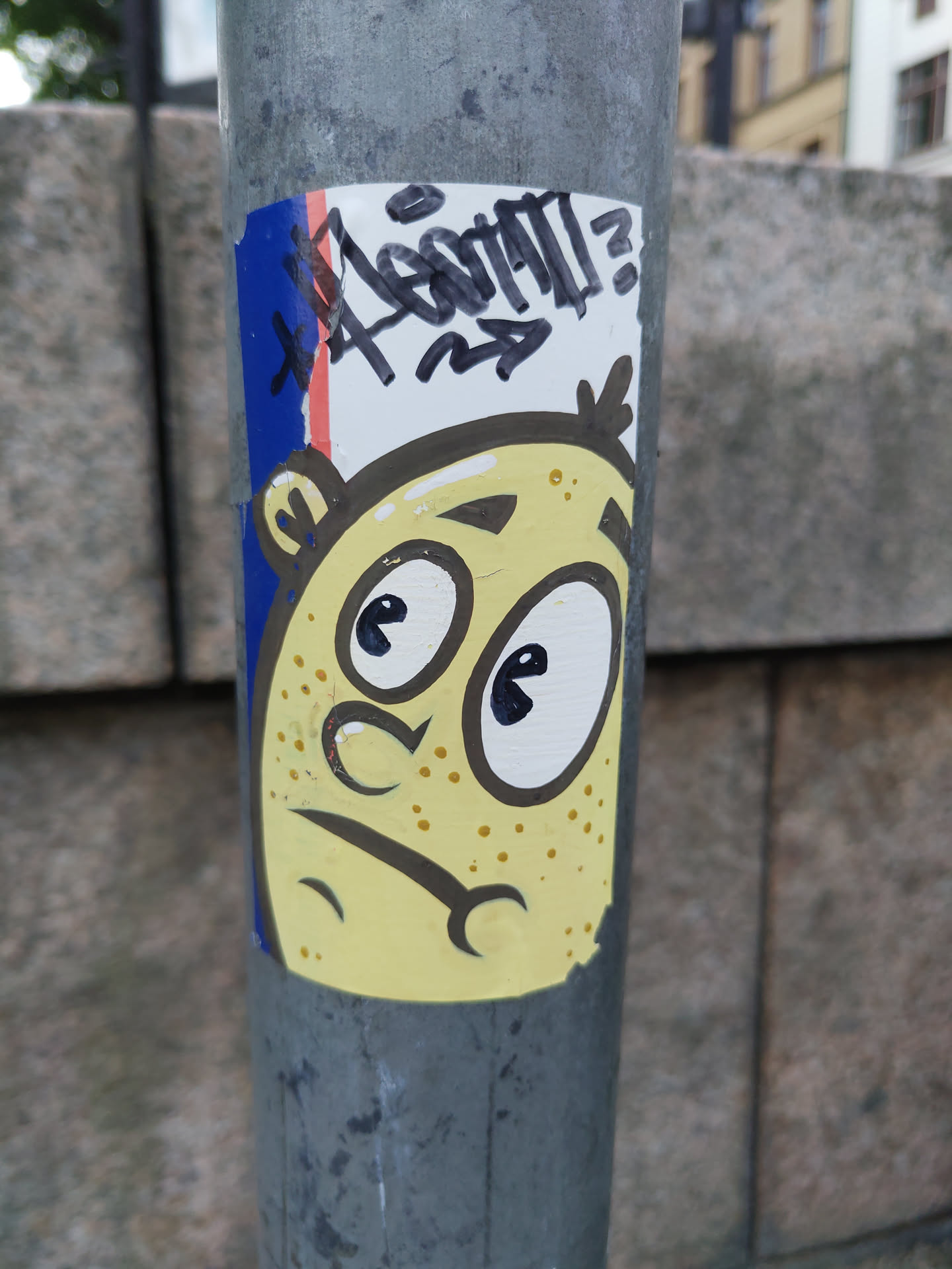The sticker features a yellow cartoon character with big eyes and a slightly worried expression.  There's some additional tagging above the character in black marker.