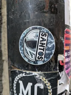 Round sticker featuring a half helmet and the word SANTOS on a camo background.