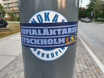 A blue and white sticker featuring the text "Sofia Läktaren Stockholm" and a small logo.  The sticker is affixed to a grey pole.