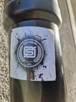Black and white sticker with a logo and the words "Secret Operations" and "Sweden". The logo is a stylized "SI" inside a circle with laurel leaves, with a grunge effect around it.