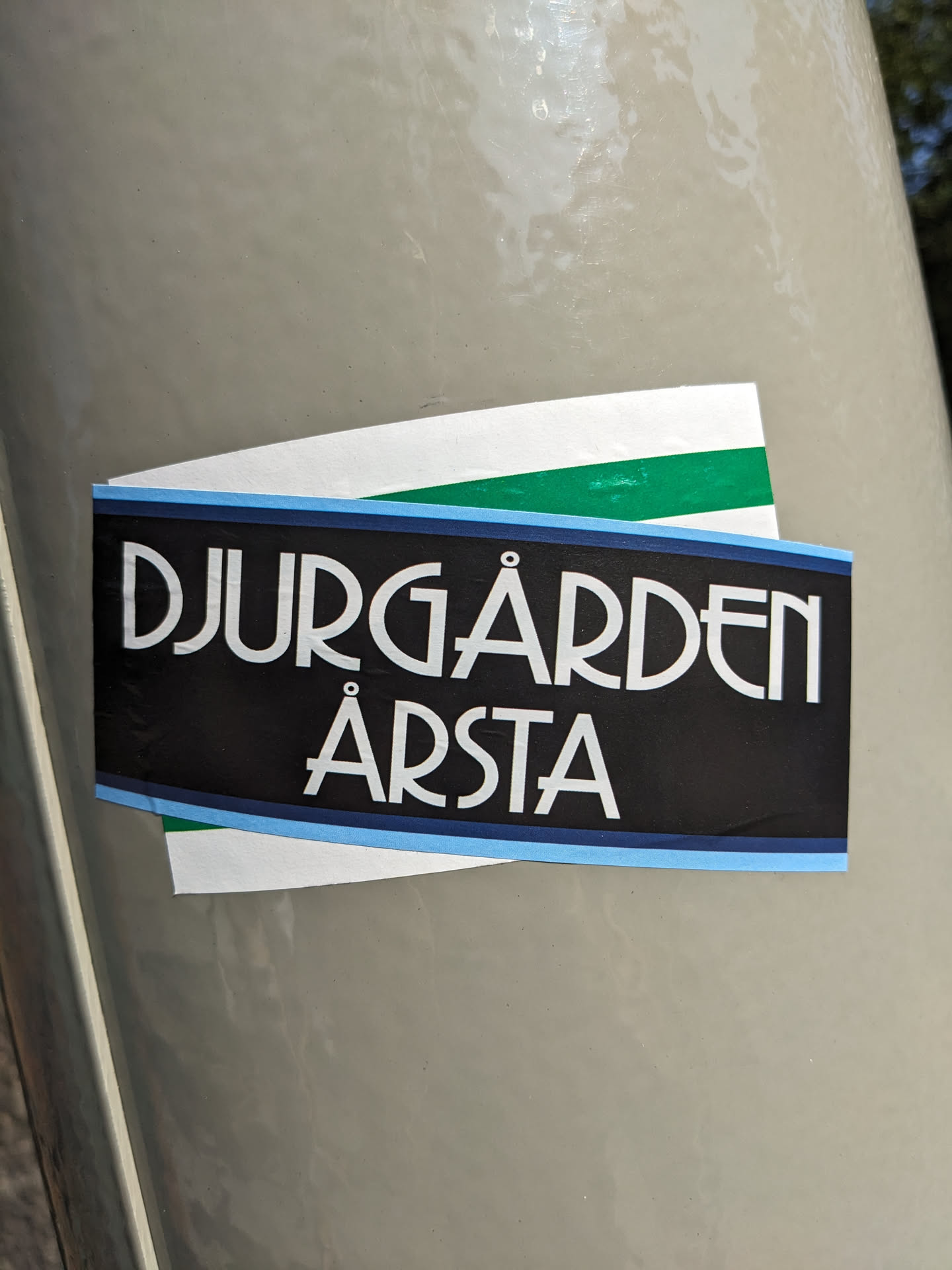 A sticker featuring the text "Djurgården Årsta" in a stylized art deco font.  The sticker is black with light blue and green accents.