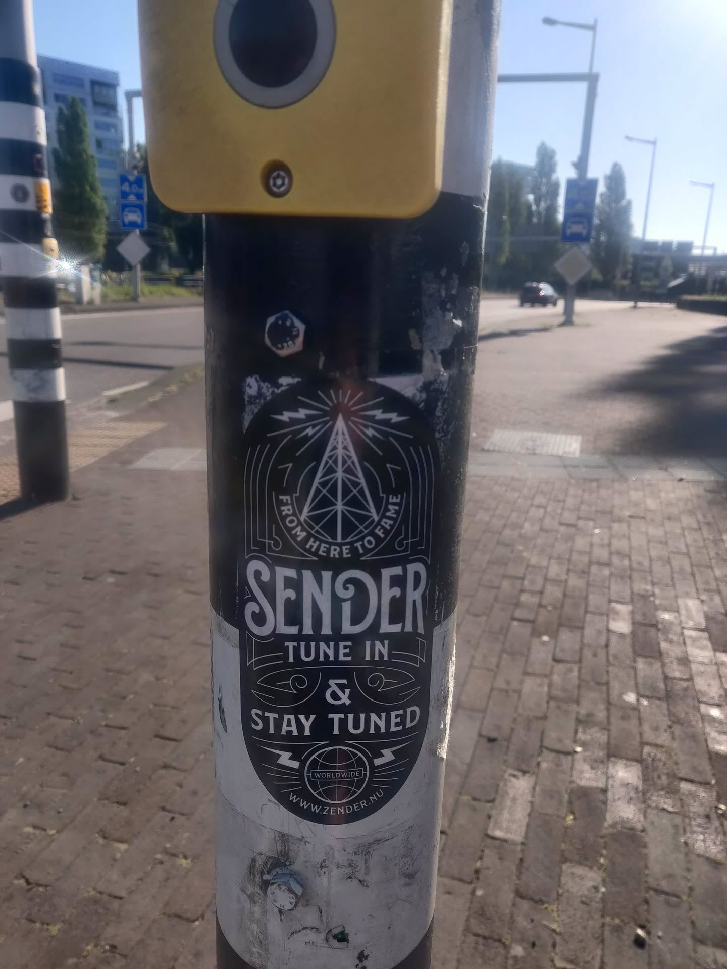 Black and white sticker with a vintage design. It features a radio tower graphic, the words "Sender", "Tune In", "&", and "Stay Tuned", and a website address at the bottom. 