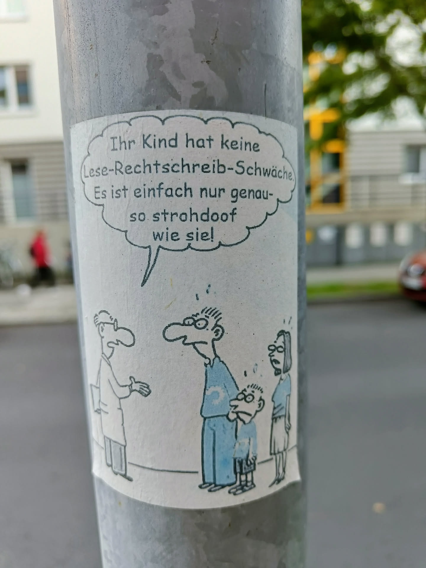 A satirical cartoon sticker depicts a family consulting a doctor. The speech bubble reveals a blunt assessment of the child's literacy struggles. The style is simple, with bold lines and minimalist coloring.