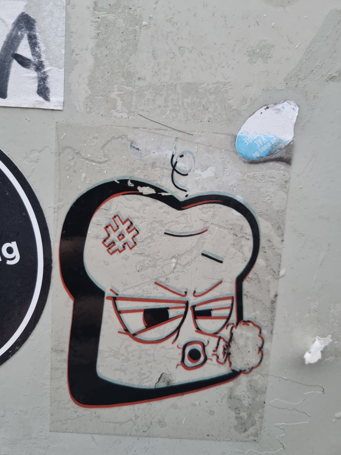 A sticker featuring a cartoon illustration of a slice of bread with a grumpy expression, smoking.  The bread has a hashtag on its surface. The sticker shows some signs of wear and tear.