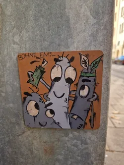 A sticker featuring three quirky cartoon characters with large eyes and simple designs. The color palette is primarily muted, with shades of grey and orange. The sticker is adhered to a grey metal pole outdoors. The artist's signature, "BOHNE EMIL," is visible at the top.