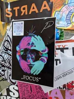 A vibrant sticker featuring a psychedelic illustration of a face surrounded by hands. The artist's signature is visible in the upper right corner, and the word "FOCUS" is written at the bottom. A QR code linking to the artist's Instagram is also included.