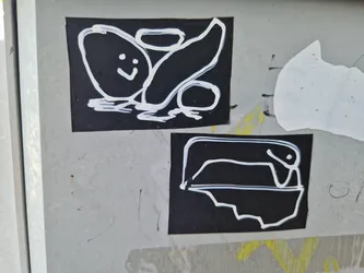 Two black stickers with simple white drawings. The top sticker shows a happy potato-like shape and a curved line. The bottom sticker depicts a simple line drawing of a creature or object in a container.  The style is childlike and playful.