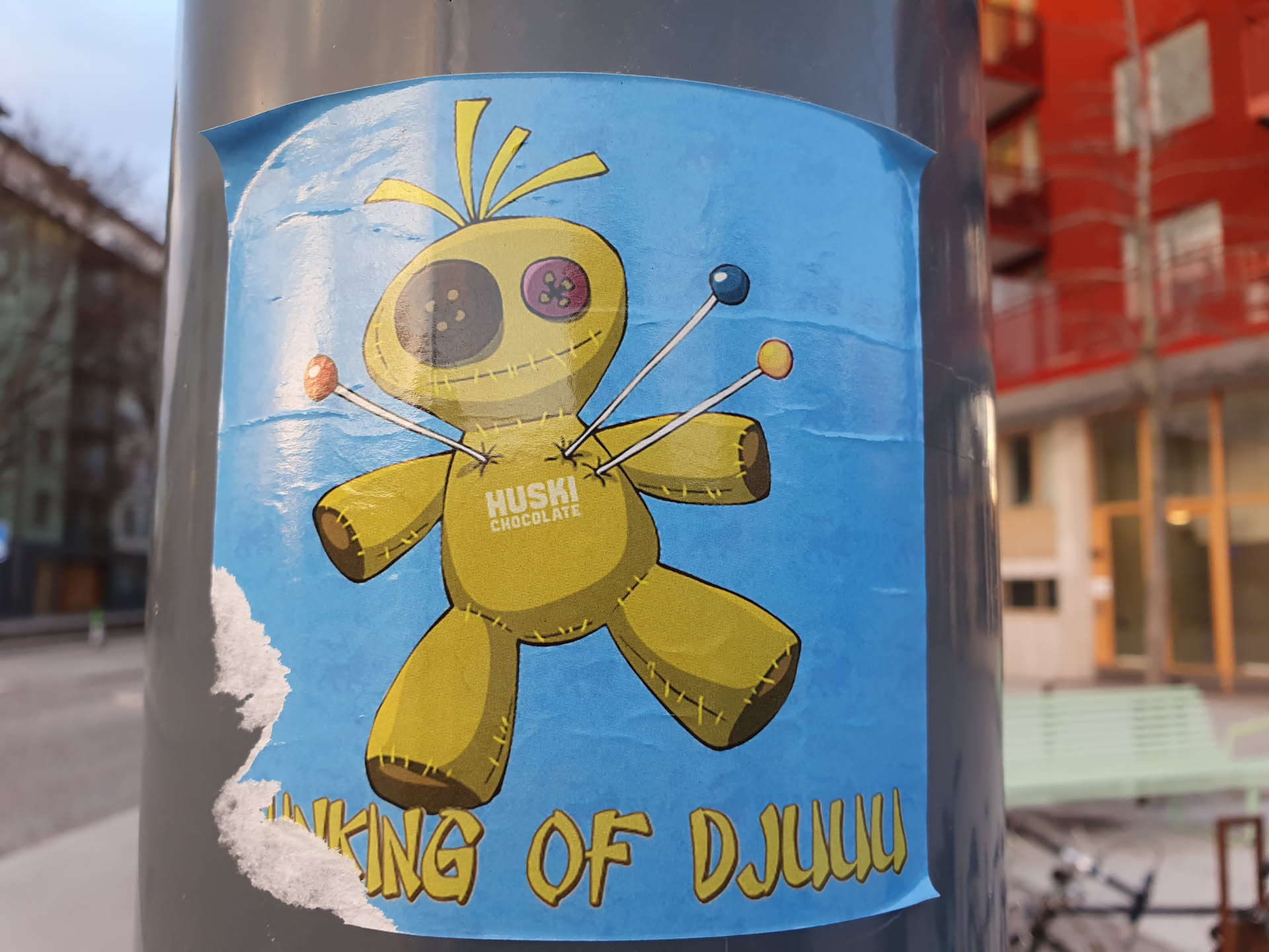 A sticker featuring a cartoon voodoo doll with pins and the text "Huski Chocolate" and "King of Djuluu". The sticker is blue and yellow and has a worn look.