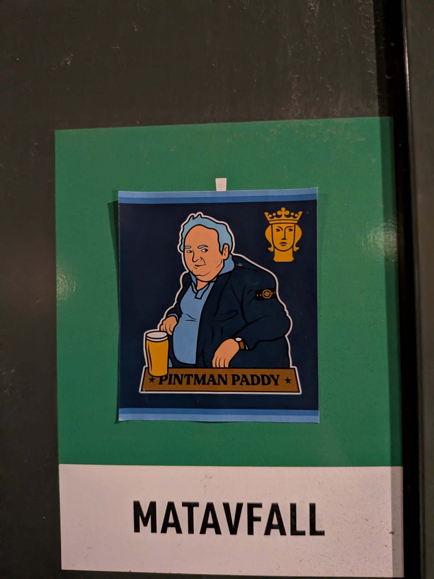 A rectangular sticker on a dark navy background framed with light blue borders at the top and bottom. It features an illustration of 'Pintman Paddy' (Paddy Losty) with light blue-grey hair, seated at a bar with a pint of beer in front of him. He is wearing a dark jacket bearing the iconic Stone Island compass badge on the sleeve. In the upper right corner sits a golden silhouette emblem of Saint Eric, the symbol of the City of Stockholm. A gold banner at the bottom contains the text '★ PINTMAN PADDY ★'.