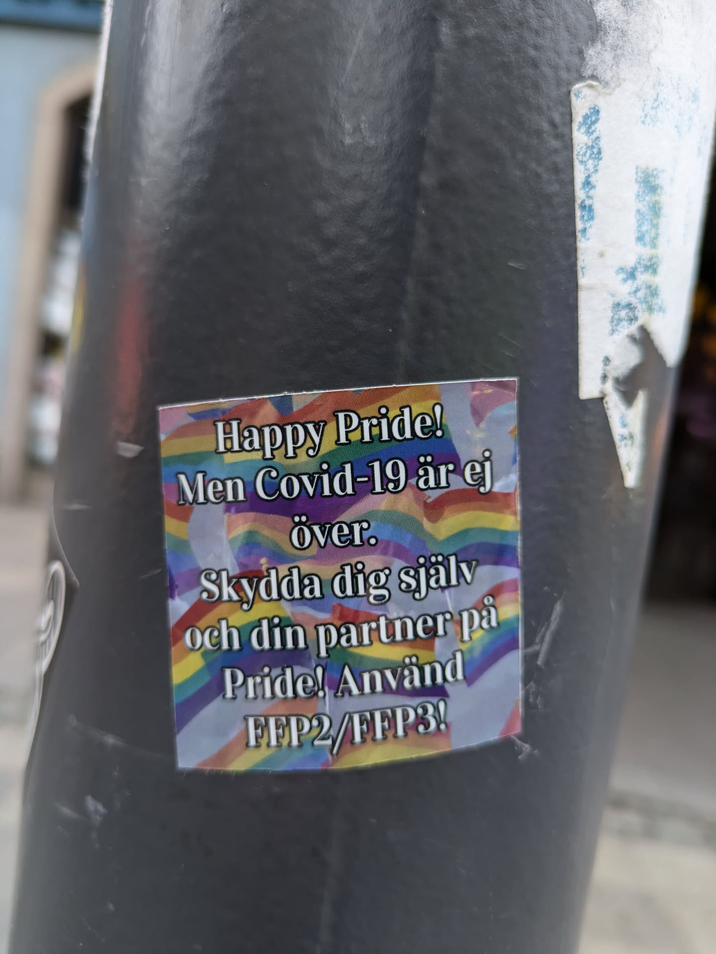 A sticker with a rainbow flag background promoting safe practices during Pride. The text is in Swedish.  It advises using FFP2/FFP3 masks to protect oneself and one's partner.