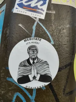 A sticker featuring a grayscale illustration of Donald Trump in a meditative pose. The text on the sticker reads: "MEDITATE IT'S HUGE!"