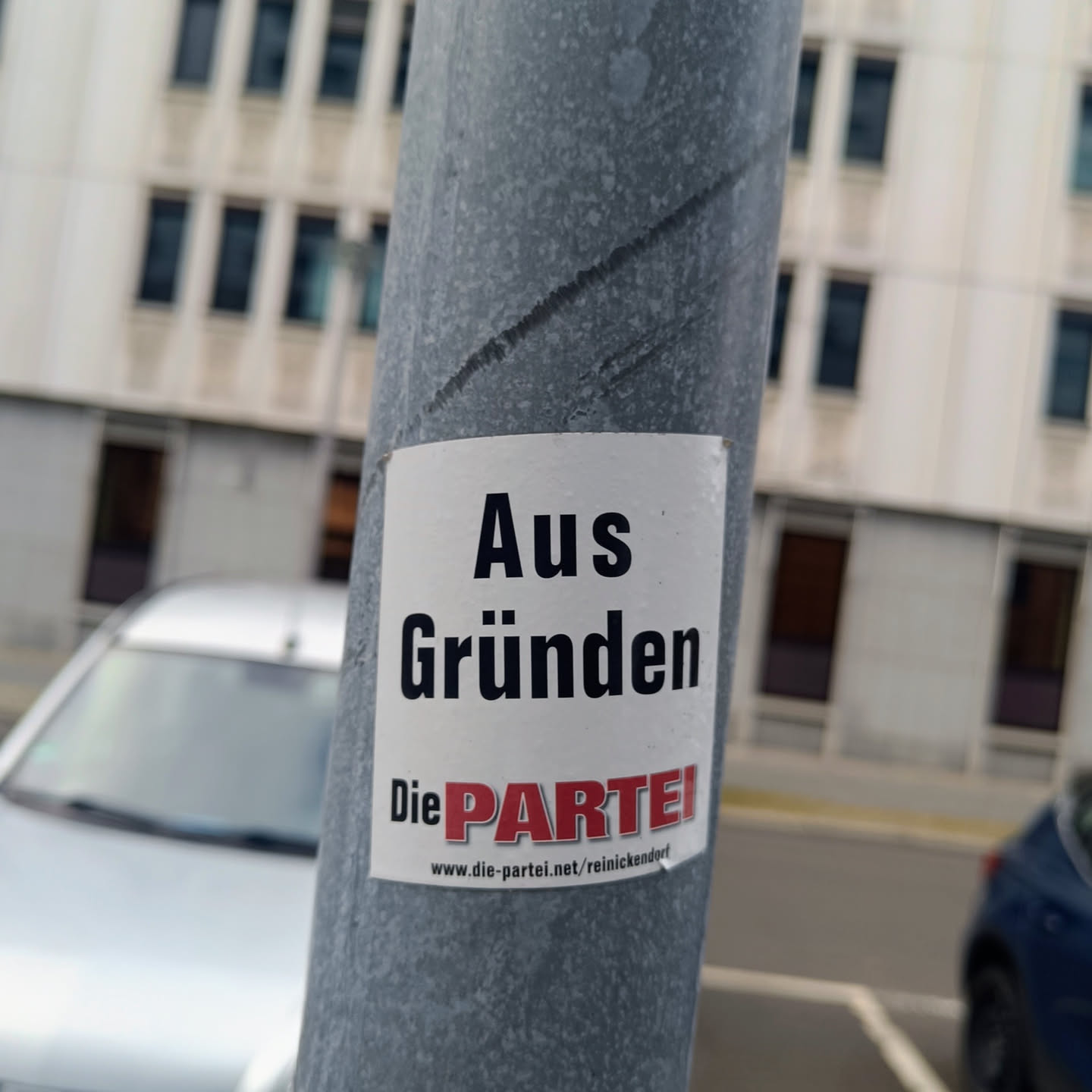 A sticker featuring the text "Aus Gründen" (For Reasons) and the logo of the German satirical party "Die PARTEI". The sticker is affixed to a gray pole.