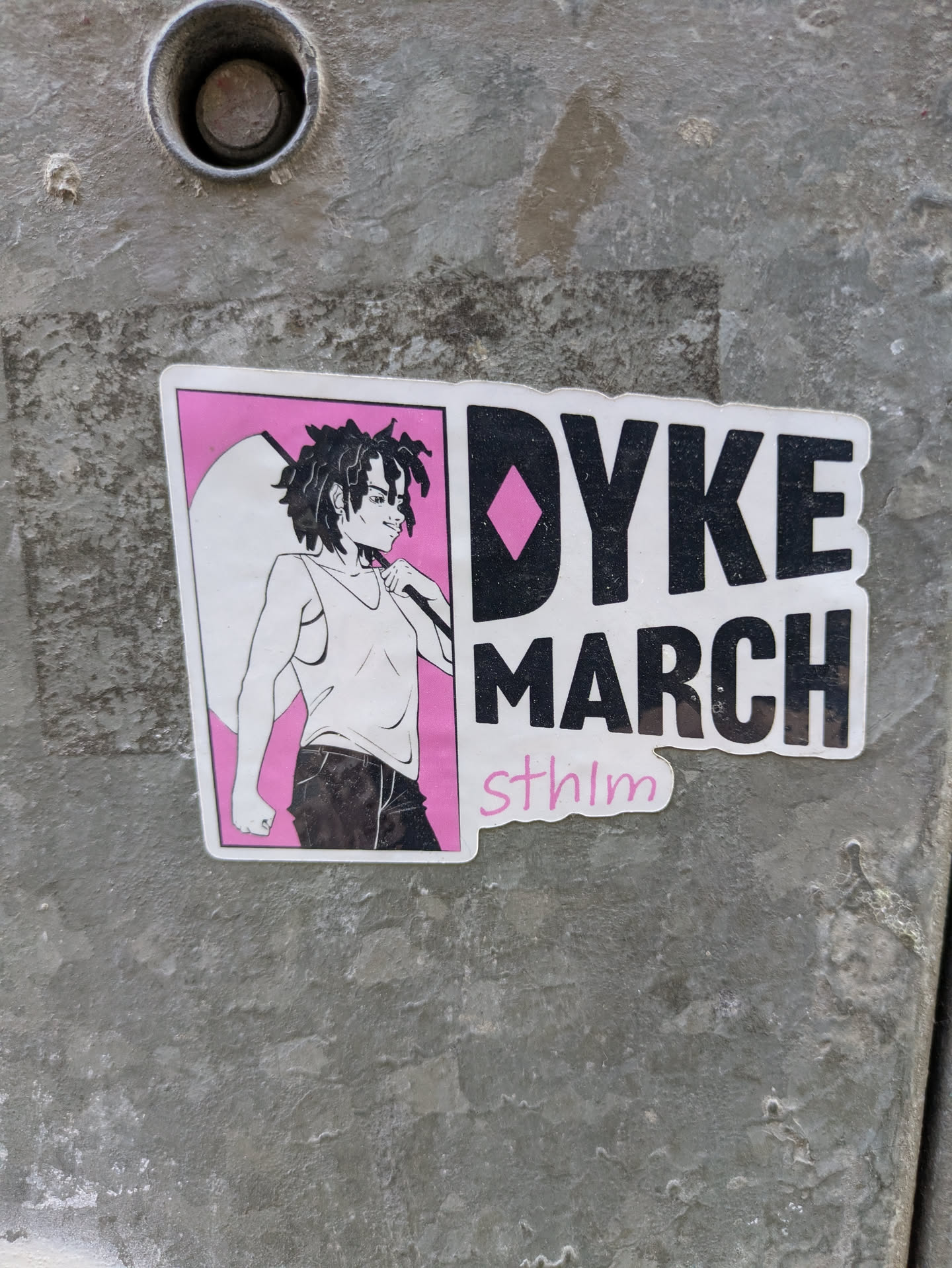 A sticker that says "Dyke March" with an illustration of a person with dreadlocks.