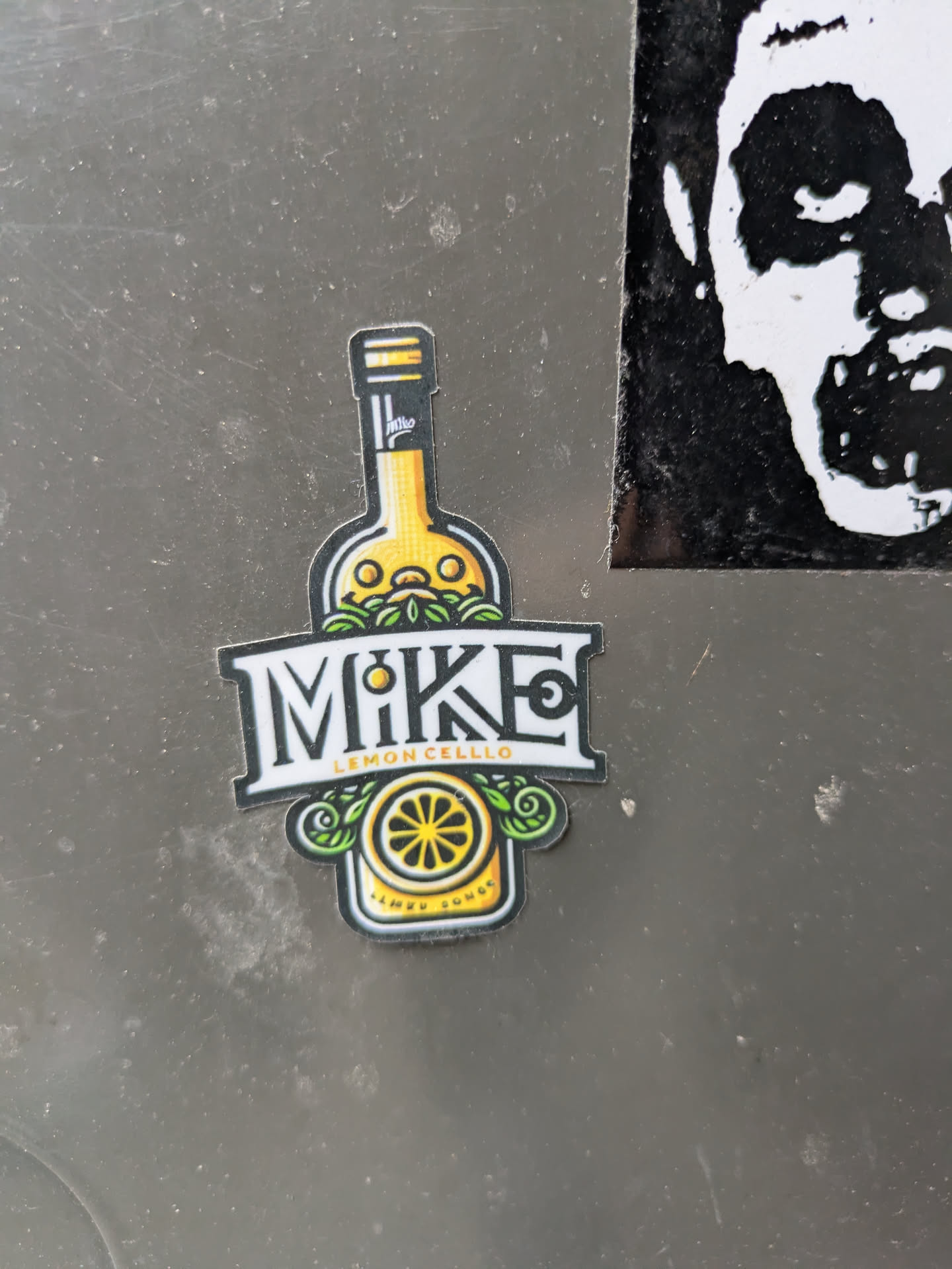A sticker featuring an illustration of a bottle of lemon cello with the word MIKE in a stylized font. The bottom of the sticker says "Lemon Sunset."