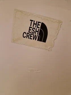 A worn-out, off-white sticker with black text and logo. The text reads "THE ESH CREW" and the logo is similar to the North Face logo.