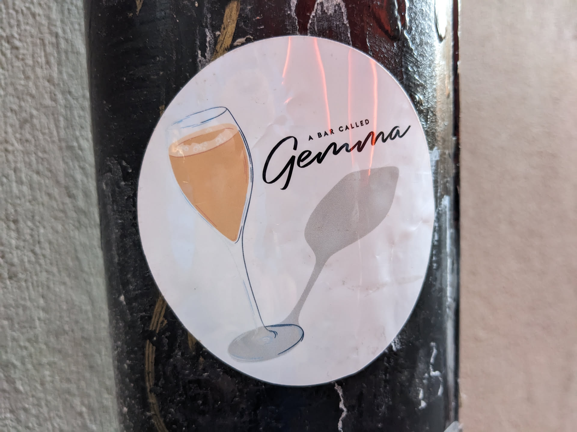Round sticker with illustration of a champagne glass and a spoon. The text 'A bar called Gemma' is written in a stylized font.